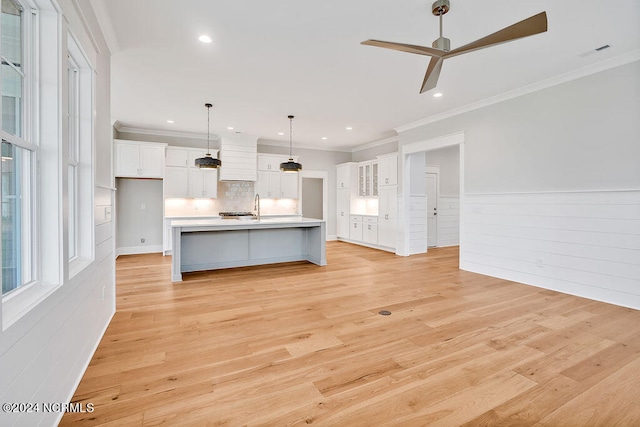 kitchen with ceiling fan, light wood-type flooring, white cabinetry, and a center island with sink