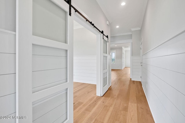 hallway featuring a barn door, ornamental molding, and light hardwood / wood-style floors