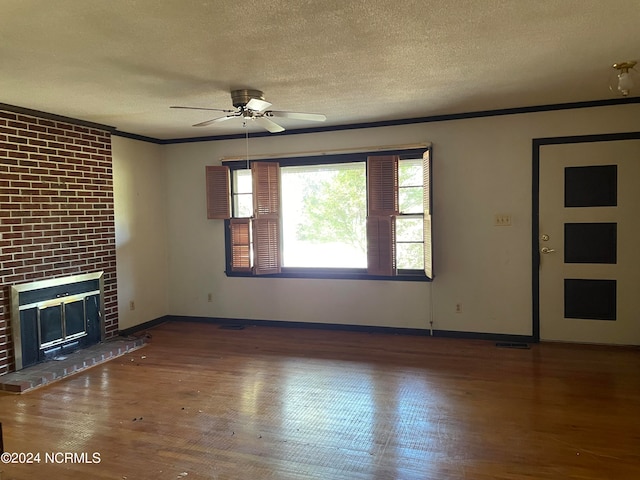 unfurnished living room with a textured ceiling, dark hardwood / wood-style floors, ornamental molding, a brick fireplace, and ceiling fan