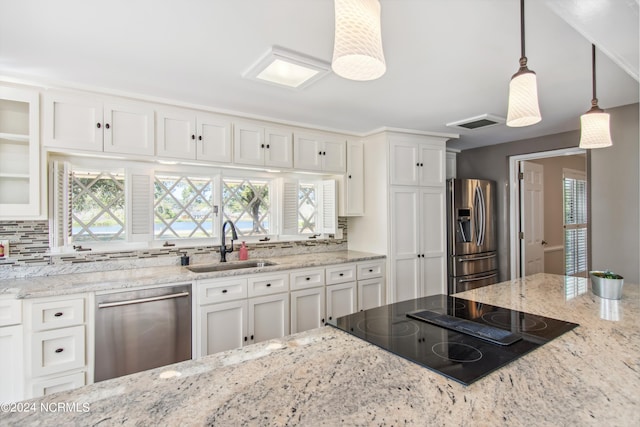 kitchen featuring appliances with stainless steel finishes, light stone counters, white cabinetry, sink, and hanging light fixtures