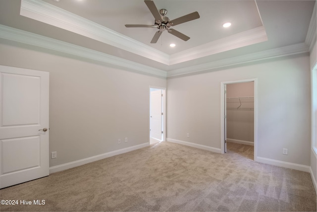 unfurnished bedroom with light carpet, a tray ceiling, a spacious closet, and ceiling fan