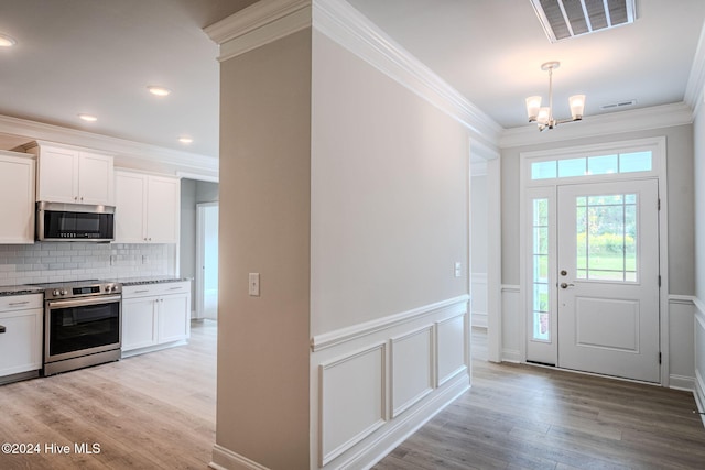 entrance foyer featuring light hardwood / wood-style flooring, ornamental molding, and a notable chandelier