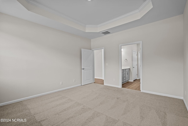 unfurnished bedroom featuring a raised ceiling, ornamental molding, light carpet, and connected bathroom