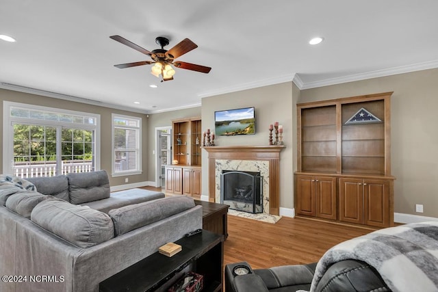 living room featuring ceiling fan, crown molding, a high end fireplace, and light wood-type flooring