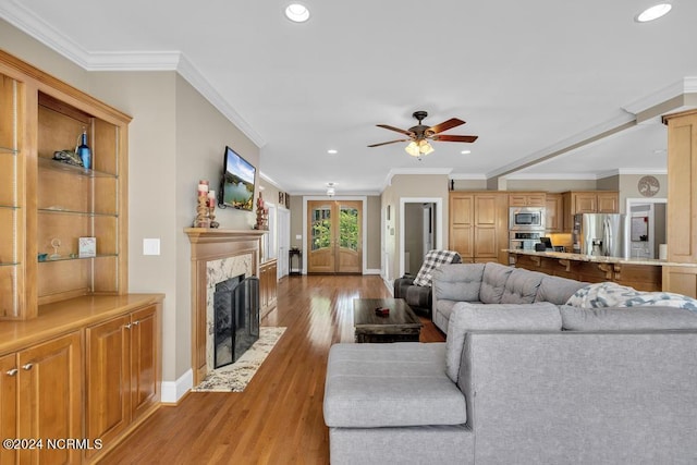 living room with ceiling fan, light hardwood / wood-style floors, ornamental molding, and a premium fireplace