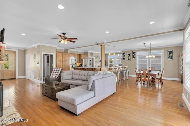 living room with ceiling fan with notable chandelier, light wood-type flooring, ornate columns, and crown molding