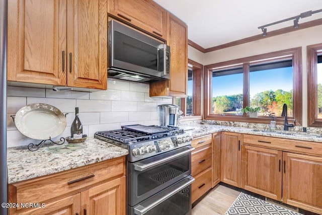 kitchen with sink, light stone counters, crown molding, backsplash, and stainless steel appliances