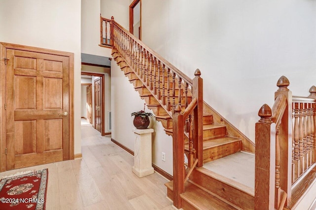 stairs featuring light wood-type flooring and a high ceiling