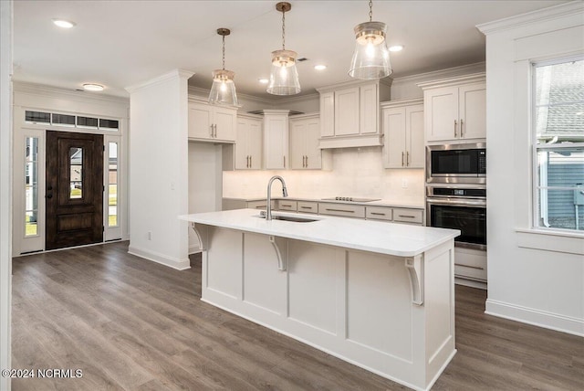 kitchen with a kitchen island with sink, dark hardwood / wood-style flooring, sink, stainless steel appliances, and hanging light fixtures