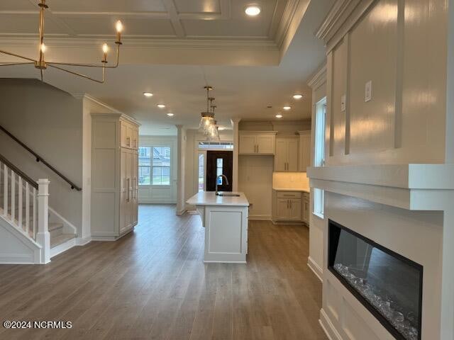 kitchen featuring a kitchen island with sink, dark wood-type flooring, decorative light fixtures, sink, and ornamental molding