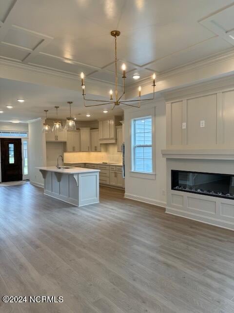 kitchen with an island with sink, hanging light fixtures, ornamental molding, a kitchen breakfast bar, and light hardwood / wood-style floors