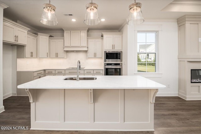 kitchen with appliances with stainless steel finishes, light stone countertops, decorative light fixtures, and a kitchen island with sink