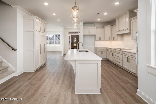 kitchen with crown molding, hardwood / wood-style floors, a center island with sink, decorative light fixtures, and sink