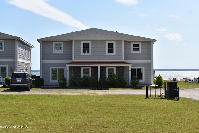 rear view of house featuring a water view, a lawn, dirt driveway, and roof with shingles