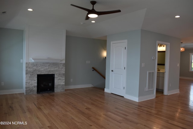 unfurnished living room featuring a stone fireplace, ceiling fan, hardwood / wood-style flooring, and vaulted ceiling