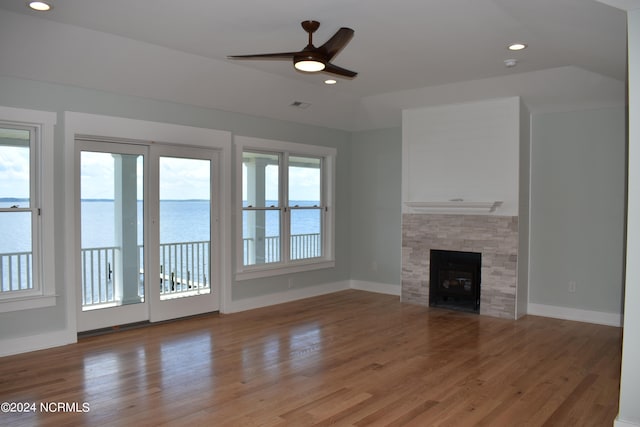 unfurnished living room featuring plenty of natural light, a stone fireplace, a water view, and wood-type flooring