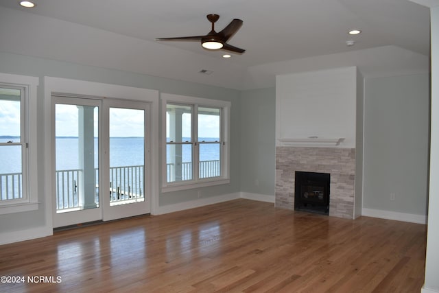 unfurnished living room featuring light wood-style flooring, recessed lighting, a water view, a fireplace, and vaulted ceiling