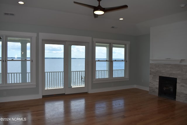 unfurnished living room with a water view, plenty of natural light, a stone fireplace, and dark hardwood / wood-style floors