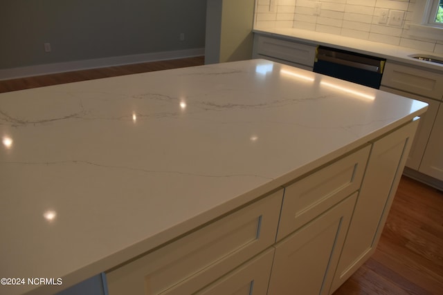 kitchen with dark hardwood / wood-style flooring, light stone countertops, tasteful backsplash, and dishwasher