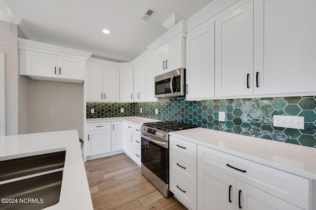 kitchen featuring white cabinets, appliances with stainless steel finishes, backsplash, and light wood-type flooring