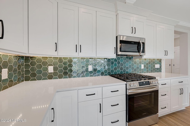 kitchen featuring white cabinets, decorative backsplash, ornamental molding, appliances with stainless steel finishes, and light hardwood / wood-style floors