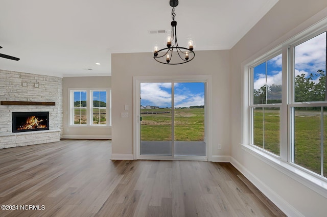 unfurnished dining area featuring a fireplace, light wood-type flooring, and ceiling fan with notable chandelier