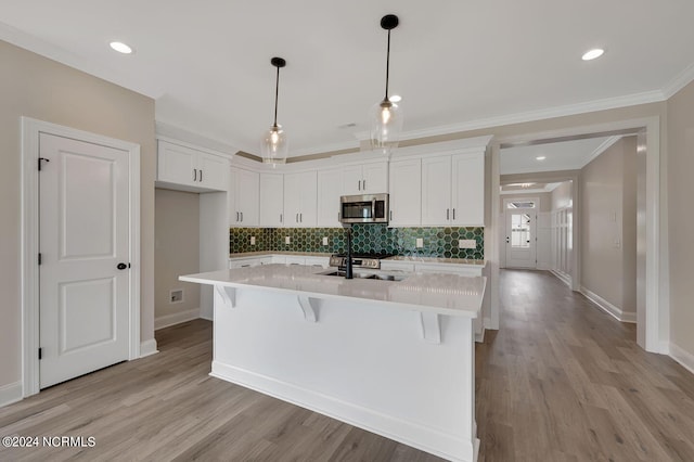 kitchen featuring light wood-type flooring, white cabinetry, hanging light fixtures, and an island with sink