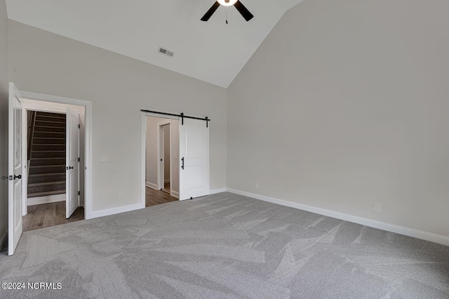 unfurnished bedroom with carpet flooring, ceiling fan, a barn door, high vaulted ceiling, and a spacious closet