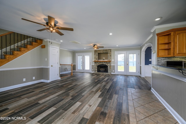 unfurnished living room with french doors, ceiling fan, ornamental molding, dark hardwood / wood-style flooring, and a stone fireplace