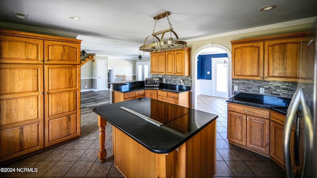 kitchen with backsplash, ceiling fan with notable chandelier, a kitchen breakfast bar, a kitchen island, and dark tile flooring