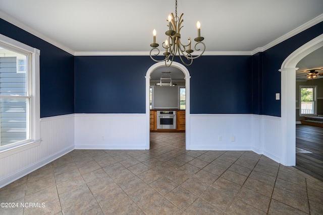 empty room featuring dark tile floors, ceiling fan with notable chandelier, and crown molding