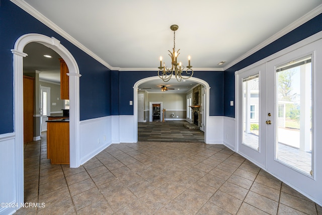 unfurnished dining area with french doors, ceiling fan with notable chandelier, a stone fireplace, and tile flooring