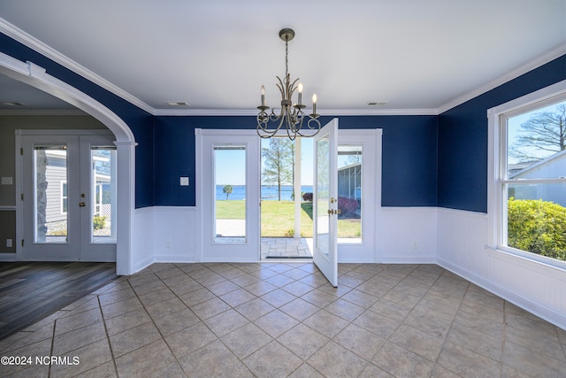 empty room featuring light tile floors, a notable chandelier, french doors, and crown molding