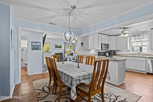 dining space featuring ornamental molding, ceiling fan with notable chandelier, sink, and light hardwood / wood-style flooring