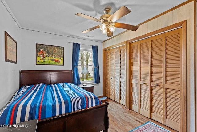 bedroom with crown molding, ceiling fan, multiple closets, and light hardwood / wood-style flooring