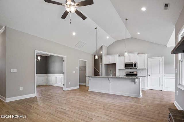 kitchen with a kitchen bar, white cabinetry, appliances with stainless steel finishes, an island with sink, and light stone countertops