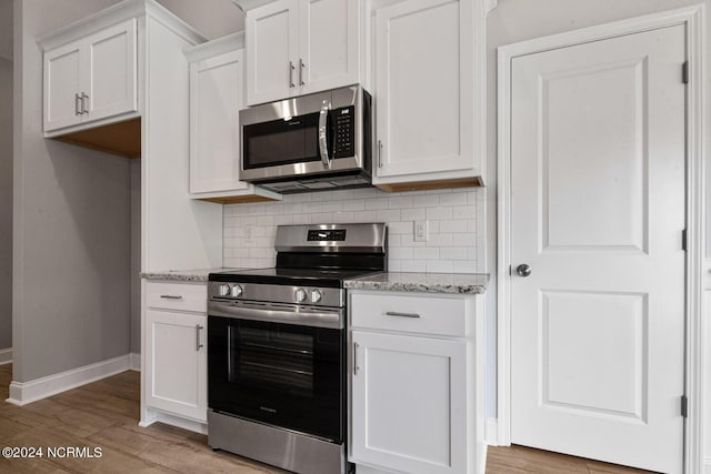 kitchen with white cabinets, decorative backsplash, light stone counters, stainless steel appliances, and light hardwood / wood-style flooring