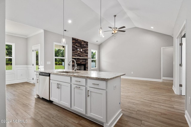 kitchen featuring decorative light fixtures, white cabinetry, sink, stainless steel dishwasher, and a center island with sink