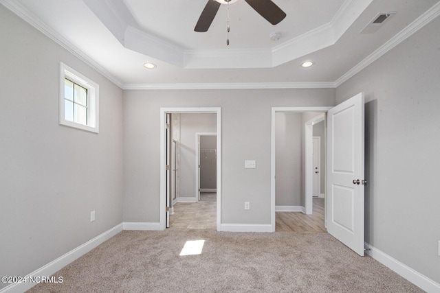 unfurnished bedroom featuring a walk in closet, light colored carpet, ornamental molding, a raised ceiling, and ceiling fan