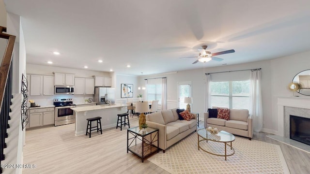 living room featuring ceiling fan, a high end fireplace, and light hardwood / wood-style flooring