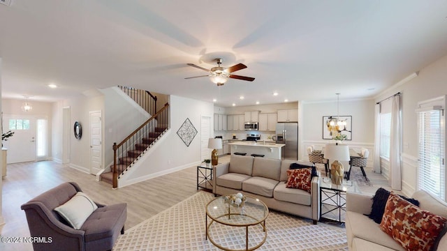 living room featuring ceiling fan with notable chandelier, light hardwood / wood-style flooring, and ornamental molding