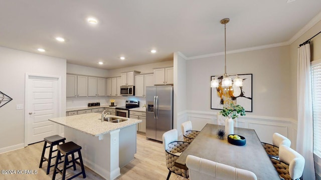 kitchen with sink, stainless steel appliances, a center island with sink, decorative light fixtures, and light wood-type flooring