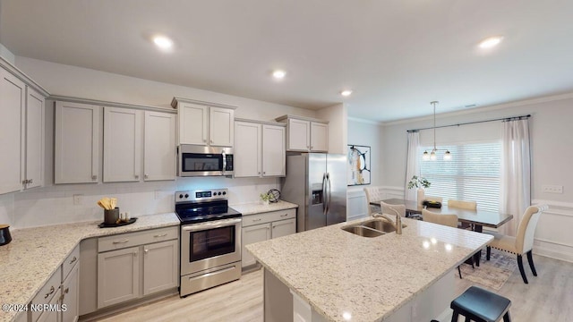 kitchen with sink, appliances with stainless steel finishes, light stone counters, light hardwood / wood-style floors, and an island with sink