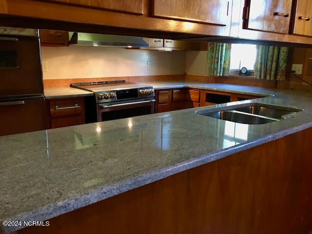 kitchen featuring high end stainless steel range, ventilation hood, double wall oven, and light stone counters