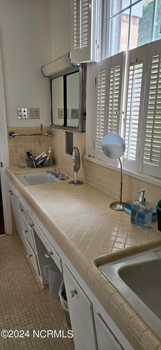 interior space with backsplash, tile countertops, white cabinetry, and sink