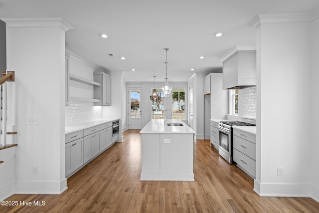 kitchen with decorative backsplash, ornamental molding, pendant lighting, stainless steel gas range oven, and an island with sink