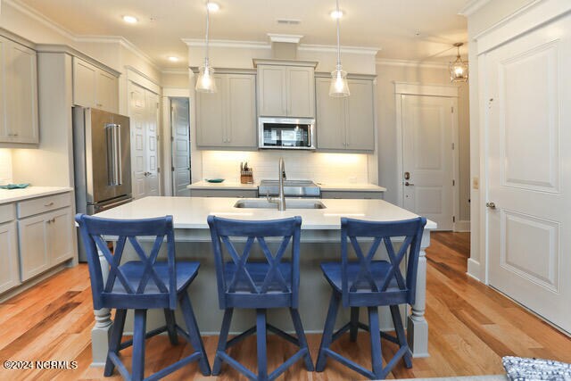 kitchen with gray cabinetry, an island with sink, hanging light fixtures, and stainless steel appliances