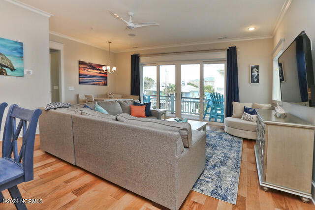 living room featuring light wood-type flooring, ornamental molding, and ceiling fan with notable chandelier