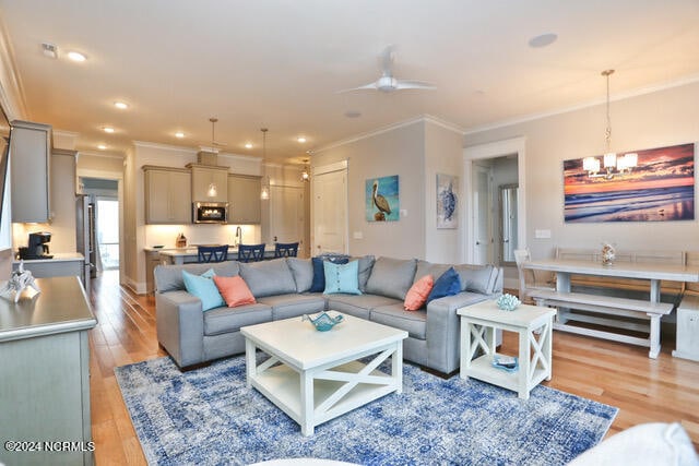 living room featuring ornamental molding, light hardwood / wood-style floors, and ceiling fan with notable chandelier