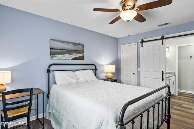 bedroom with a barn door, connected bathroom, ceiling fan, and dark hardwood / wood-style floors